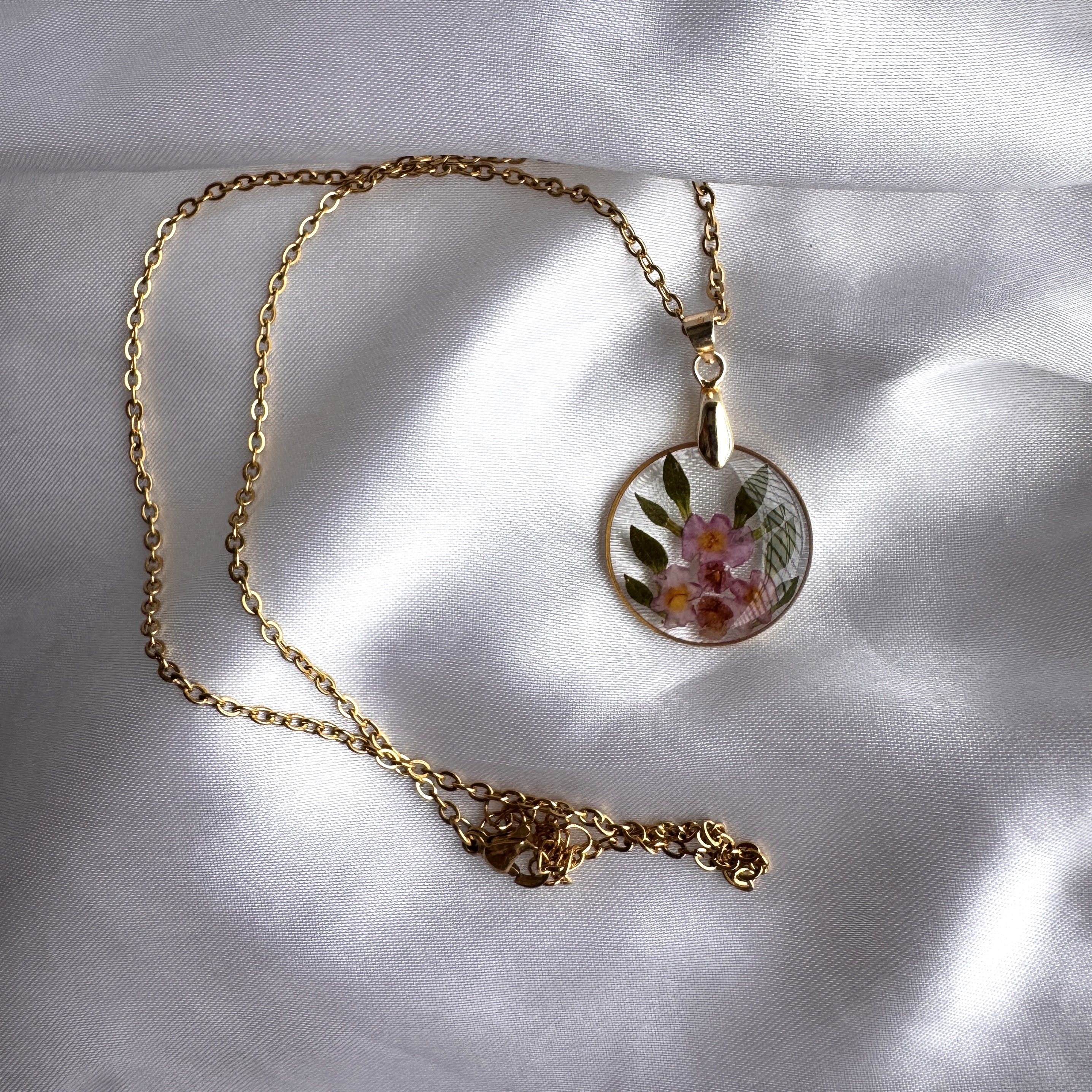 The Arch Bloom Pendant showing five violet flowers preserved in resin inside a tall golden arch.