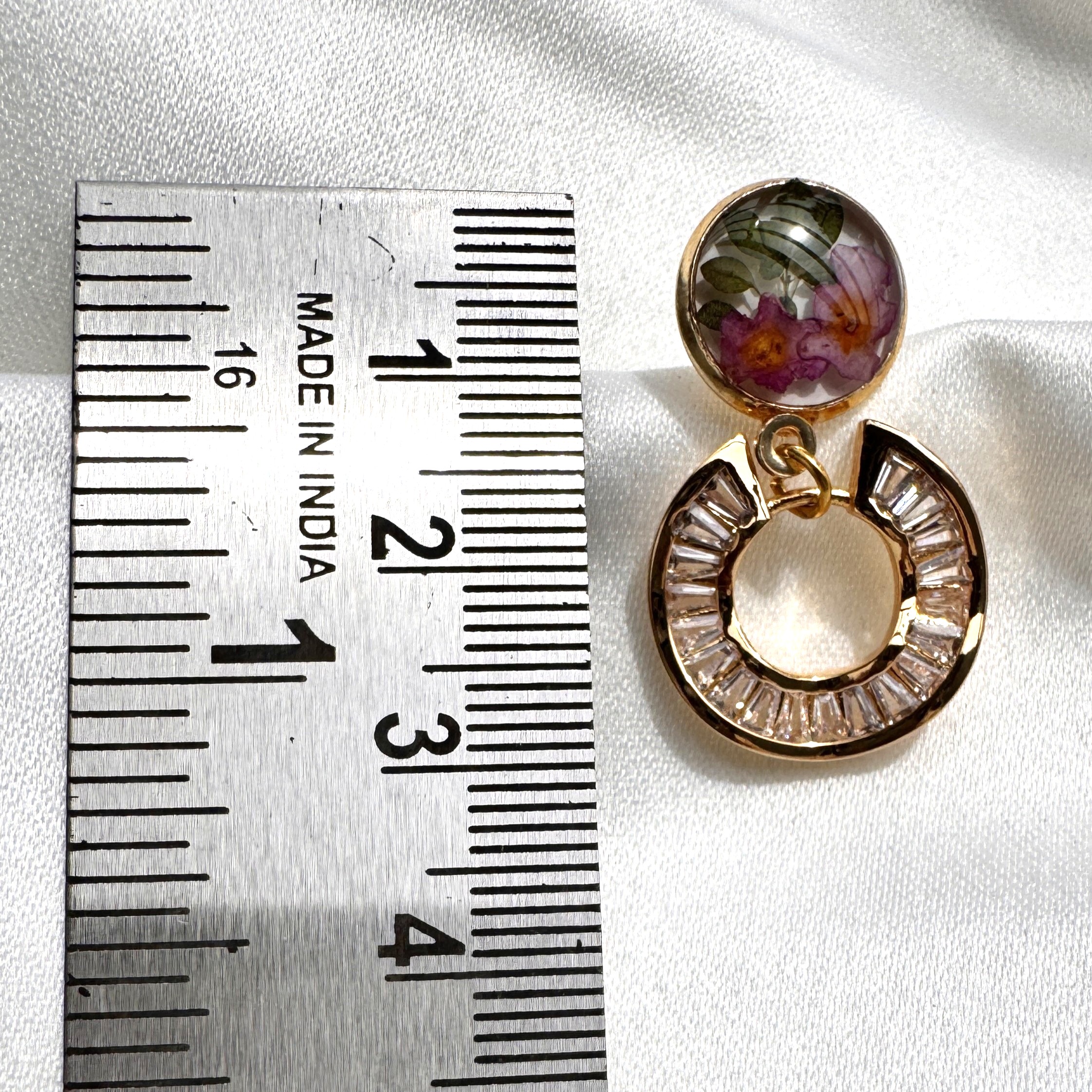 A pair of Blossom Gleam earrings with pressed violet flowers and a circular stud of baguette crystals.