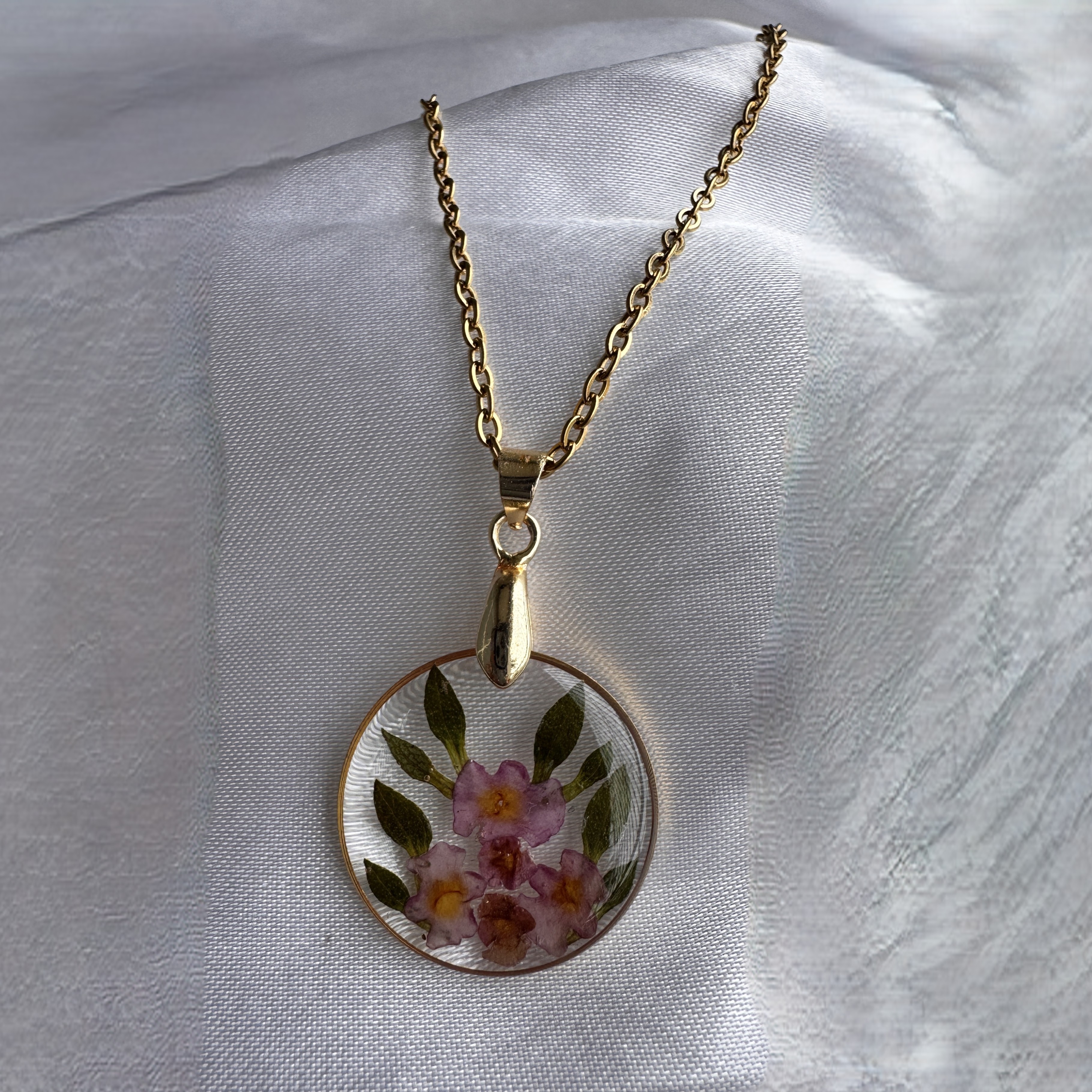 A round Floral Embrace pendant with five purple flowers and leaves preserved in resin.