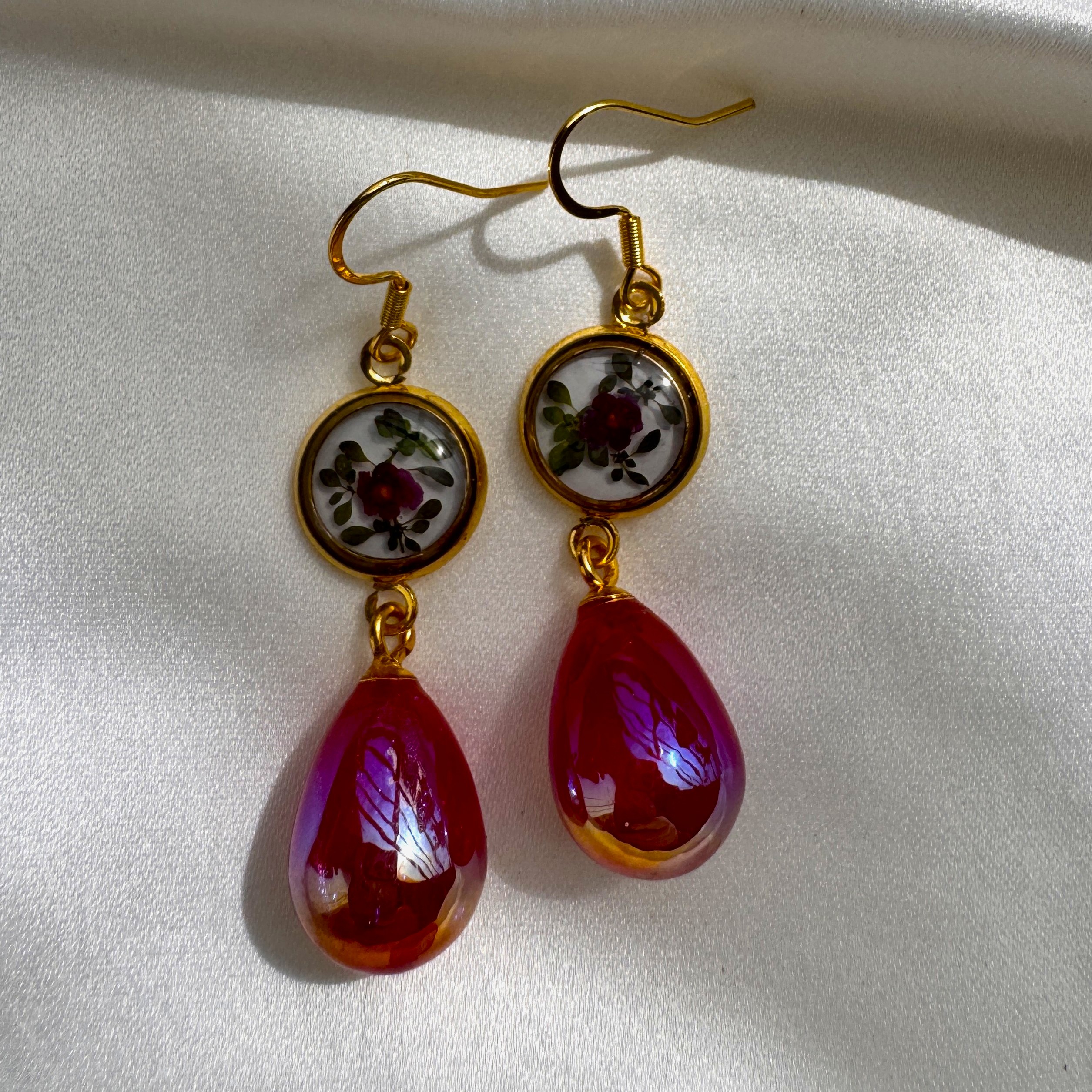 A pair of Ruby Bloom earrings with crimson petals in resin and a bold ruby red glass drop.