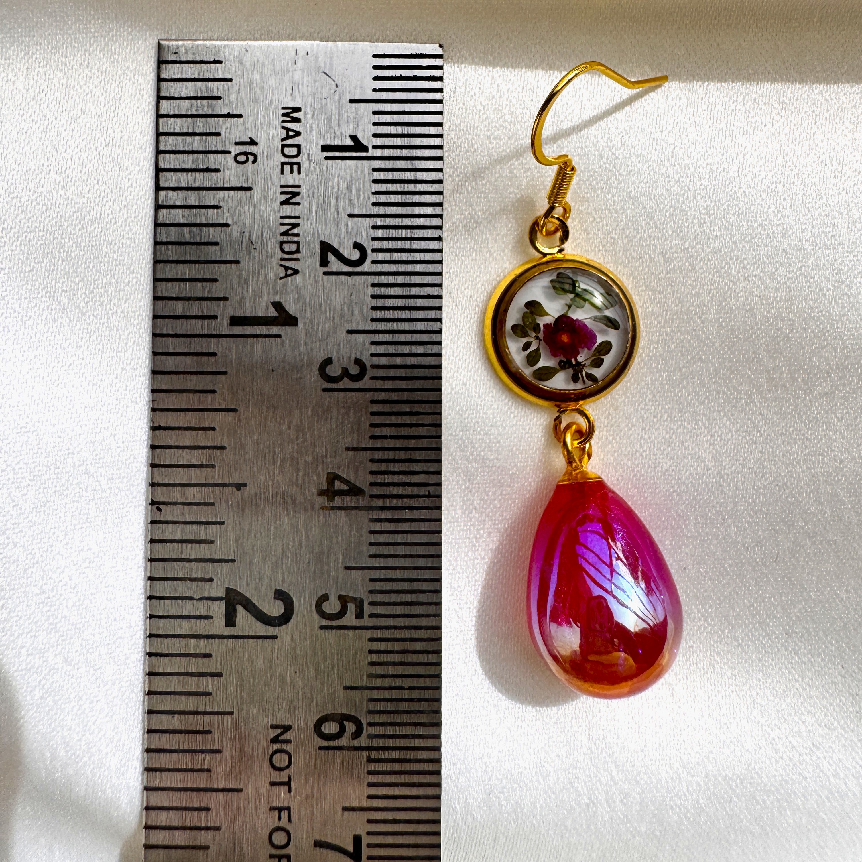A pair of Ruby Bloom earrings with crimson petals in resin and a bold ruby red glass drop.