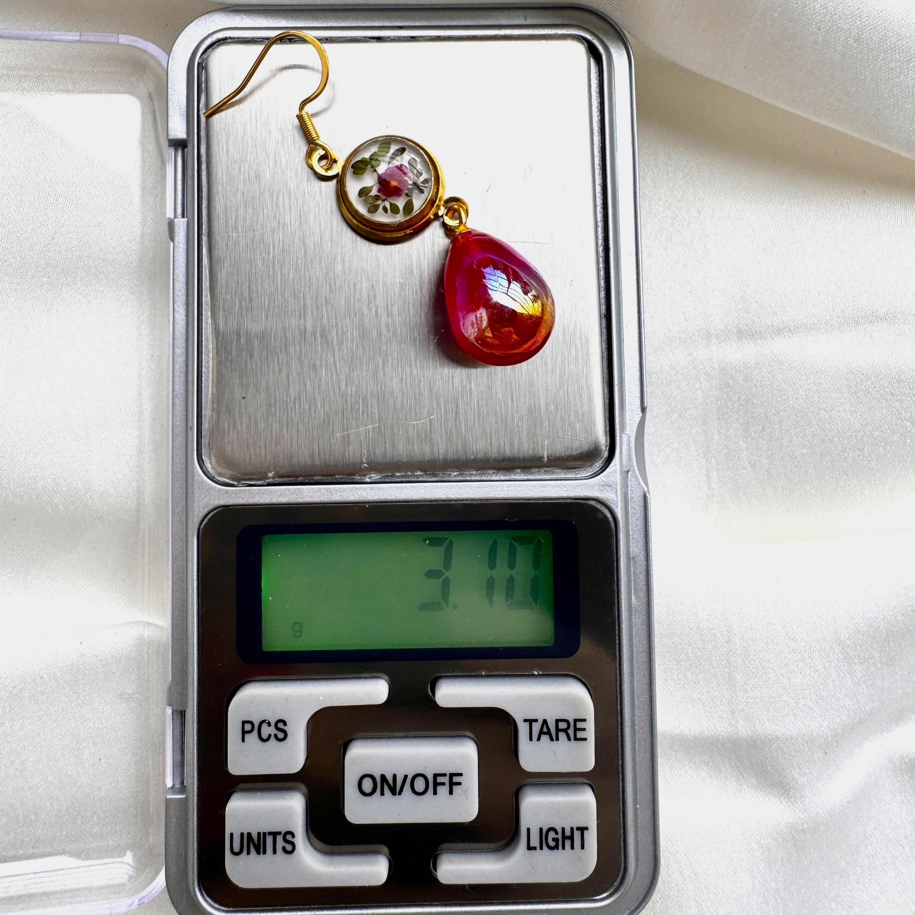 A pair of Ruby Bloom earrings with crimson petals in resin and a bold ruby red glass drop.