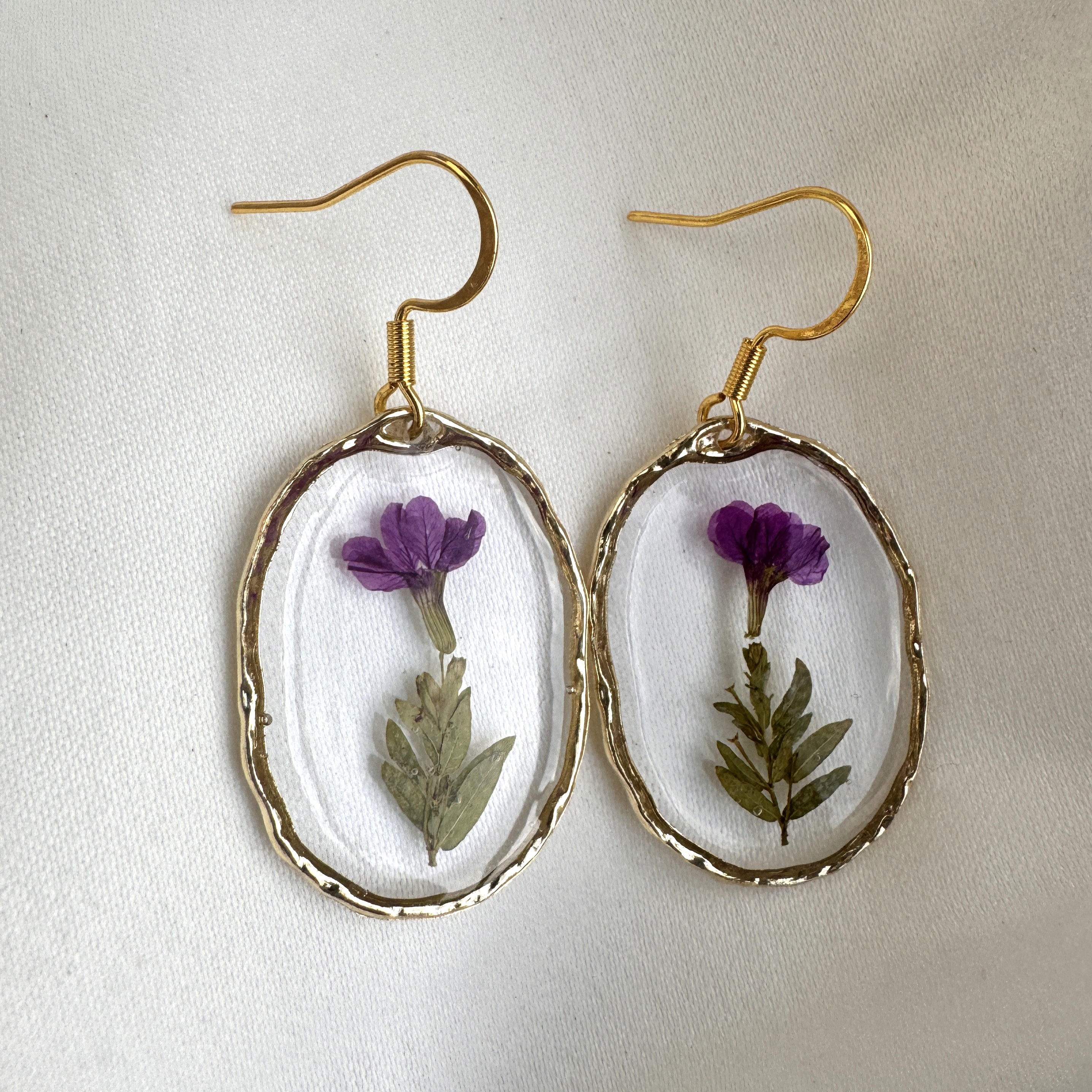 A pair of Wildflower Unity Earrings with a pressed purple flower in an organic gold frame.